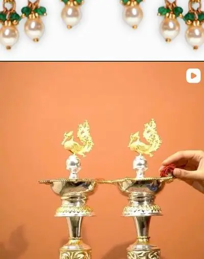 A pair of peacock deepa lamps on a terracotta ground.