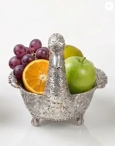 A carved silver swan bowl holding fruit.